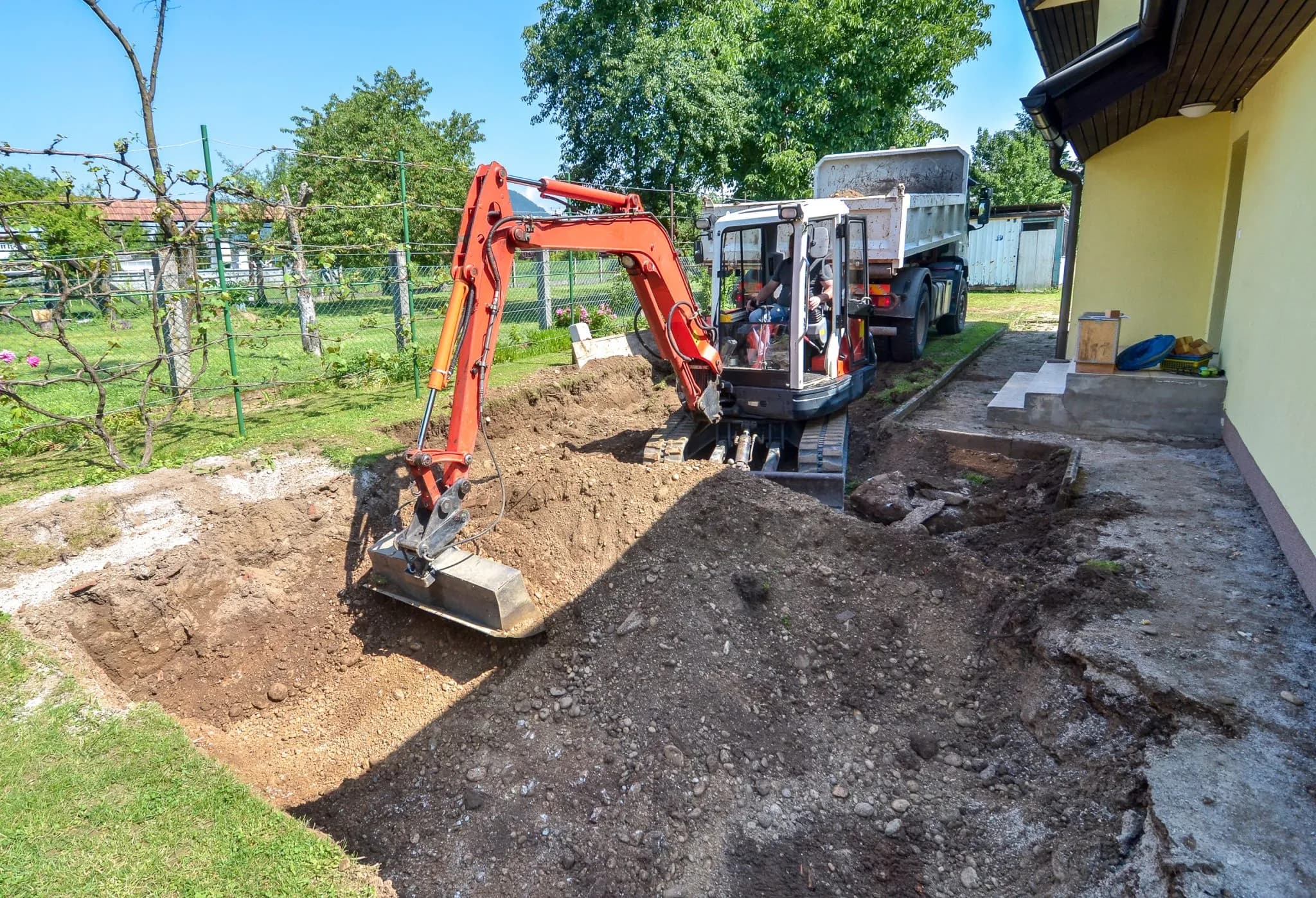 Mini excavator digging foundation next to residential home