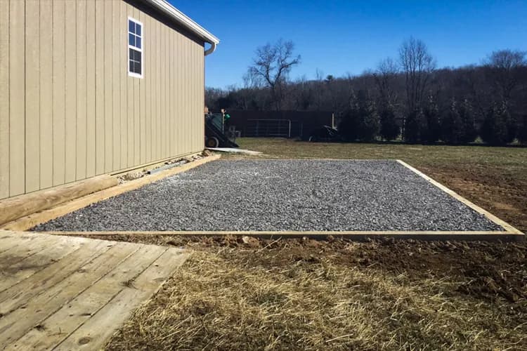 Compacted gravel pad installed next to large outbuilding