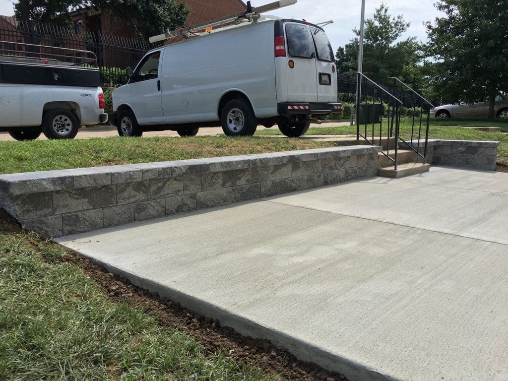 Stone block retaining wall with broom-finish concrete pad and steps